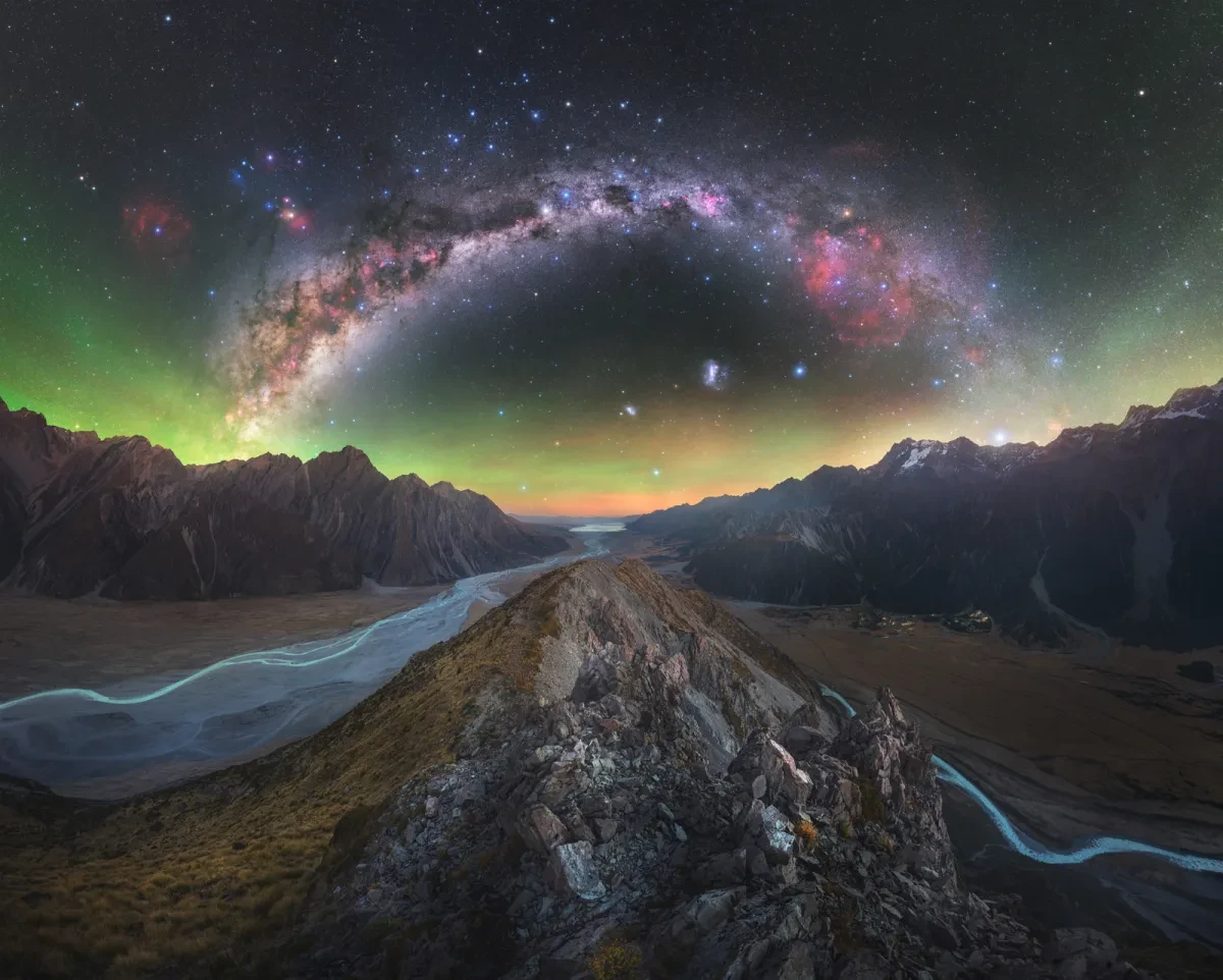 The Milky Way arches above rocky ridges, mountains and winding river tributaries.